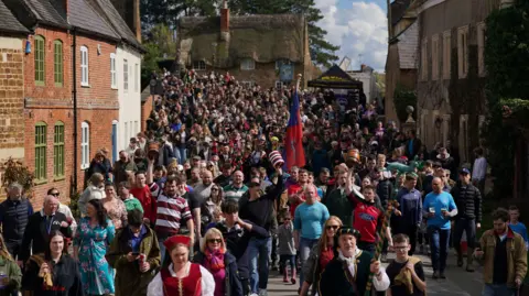 PA Media A street filled with people led by a man and a woman in medieval looking attire