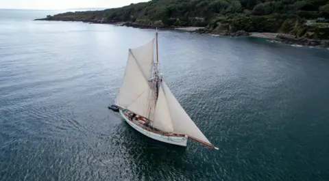 Turn to Starboard An ariel shot of the Pellew. It is a large ship with two large sails. The base of the boat is white. 