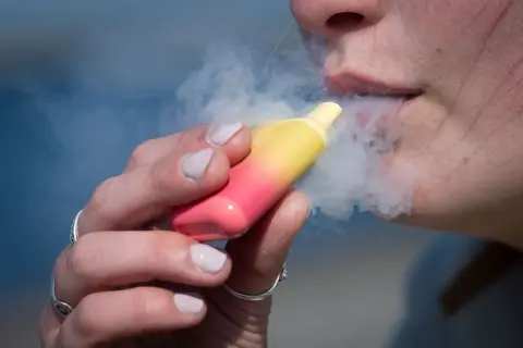 Getty Images A close up of a person smoking from a pink and yellow disposable vape