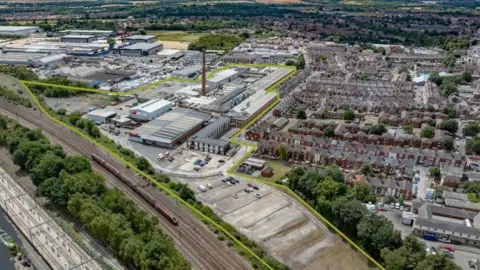 BNP Paribas Real Estate An aerial view of an industrial site surrounded by housing and a railway line, with a large chimney in the middle
