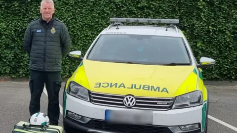 LDRS A man in an ambulance uniform stands in a parking lot next to a car with ambulance written on it