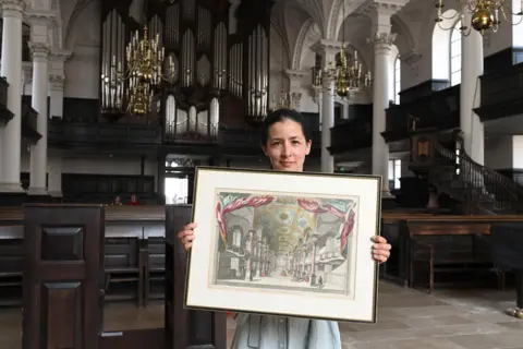 St Martin-in-the-Fields Louisa Price holding a painting of the interior the church inside St Martin's with pews columns and the organ to be seen behind her