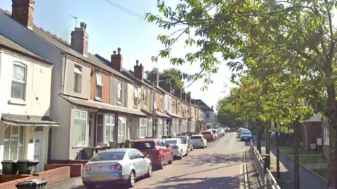 A street with terraced housing on the left and green trees on the right