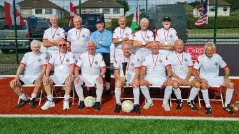 The England over-75s squad siting with their gold medals 