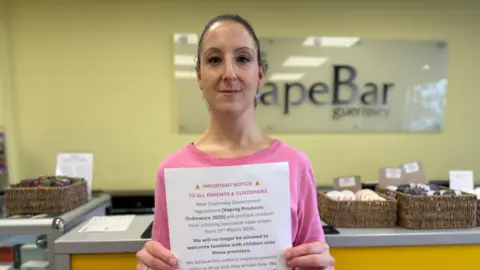 Sophie Dorfner standing infront of the till at the VapeBar. She is holding sign asking people to sign their petition. She is wearing a pink T-shirt and has dark hair.
