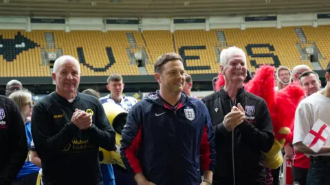 Wolves Foundation Mark Rhodes, Steve Bull and Ally Robertson stand in football kits in Molineux Stadium.