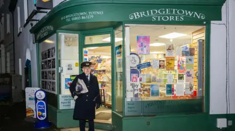 Jack Boskett A picture of a railway staff worker wearing a black hat and black jacket. He is pictured in front of a green store which reads 'Bridgetown stores'