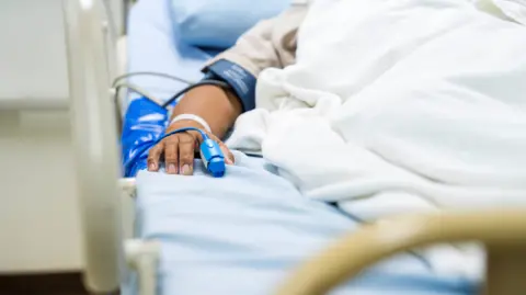 In the hospital, a patient sleeps on a bed. Heart Rate Monitor Equipment is on their finger.