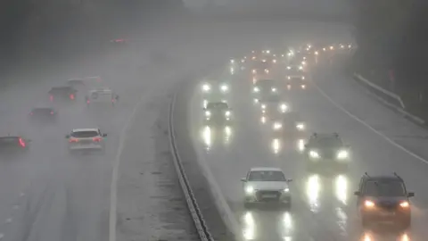 Surface water on a motorway with cars driving on it. The water is causing a glare from car headlights.