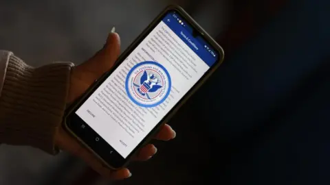 A hand holds an iPhone displaying the terms and conditions screen of the CBP's app.