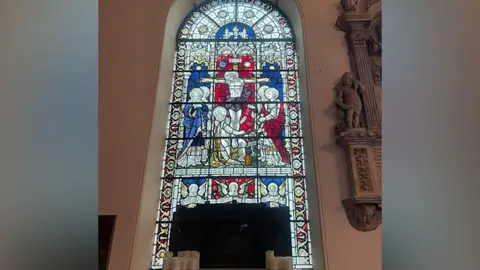 Black taped covers the bottom of a stained glass window which is blue red and yellow and depicts a scene which shows people surrounding the son of God