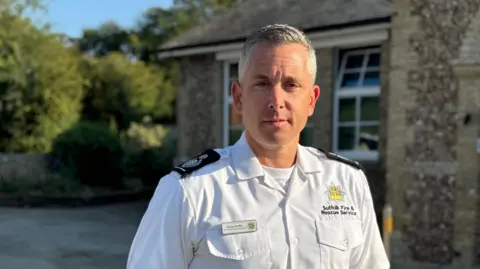 Zoie O'Brien/BBC A head and shoulders image of a firefighter. He is wearing a white shirt and looking directly into the camera. 