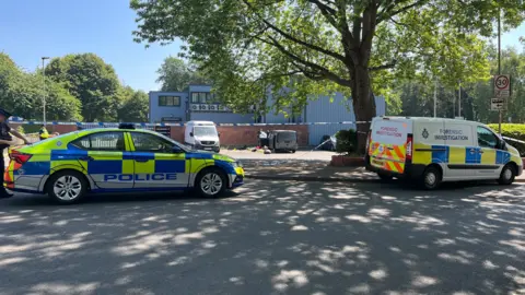 Police tape with parked vans being inspected by officers behind the cordon