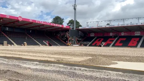 Vitality stadium with the pitch dug up and looking like sand. Two stands can be seen at an oblique angle to each other.