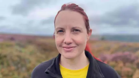 Rachel Bennett, with red hair tied in a pony tail, wearing a yellow t shirt and black fleece