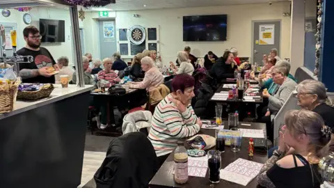 tony grant A picture of a bar where several elderly people are sat, playing bingo. 