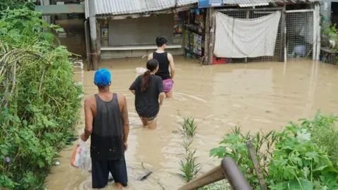 BBC/Lulu Luo Residents in the Philippines' Cabanatuan city wade through flood waters on Tuesday