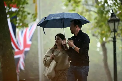 Getty Images Tourists shelter from the rain beneath umbrellas as they walk along The Mall during a torrential downpour in central London on 10 September 2025.