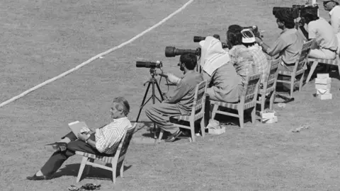Getty Images John Woodcock, on his last official tour as cricket correspondent of The Times newspaper, sits with photographers behind the boundary, during the First Test in Lahore, Pakistan, November 1987. 