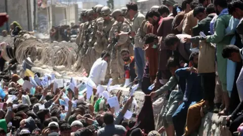 A crowd of Afghans handing their papers to soldiers at Kabul Airport