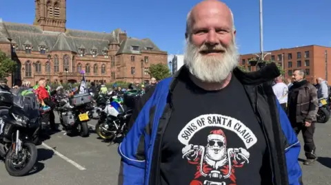 Rob Seales wearing a Sons of Santa Claus T-shirt with bikers in the background