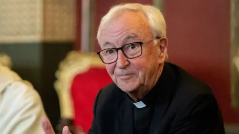 PA Media The cardinal in a black suit and clerical collar at a press conference in early 2025.