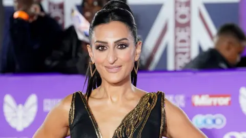 PA Punam Krishan, vêtue d'une robe glamour noire et dorée, sourit à la caméra alors qu'elle assistait aux Pride of Britain Awards à Londres