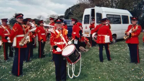 Family handout Pauline Polhill with the Wessex Military Band. She is in the centre of the frame smiling at the camera. She is in a red military jacket and hat. She is carrying a large drum.