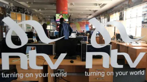 AFP via Getty Images Looking through some branded glass - with the logo of NTV on it. People in a news office can be seen in the background.