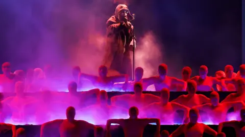 Getty Images The Weeknd pictured on-stage in a hooded jacket, while raised above a group of dancers