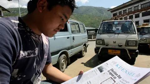 A Bhutanese map sits by a roadside in Thimphu in Bhutan reading a newspaper