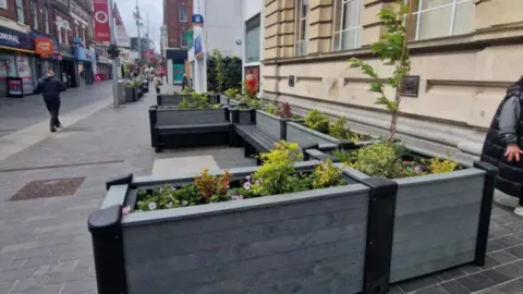 Grey planting boxes surround a large seating areas on Victoria street.