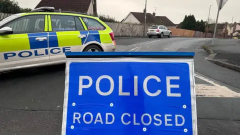 police road closed sign with police car in background at the scene of security alert