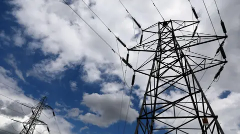 Two pylons viewed from below, against a blue sky full of white clouds.