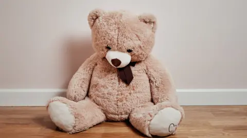 Getty Images Beige teddy bear with dark brown neck-tie sits on a wooden floor