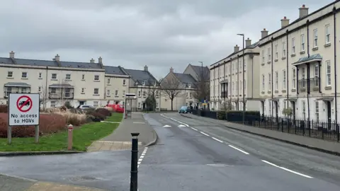 A photo showing a street lined with white town house and a number of cars parked by the side of the road