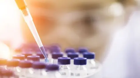 Getty Images Pipette holding a purple liquid above small bottles