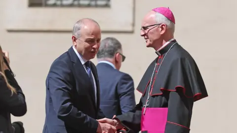 PA Media Taoiseach Michael Martin, wearing a navy suit, shaking hands with Prefect of the Papal Household Petar Rajic 