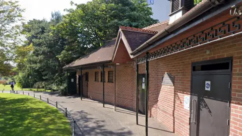 Google Street View of the brick toilet block in Bournemouth's Lower Gardens. It has a pitched, tile roof and a canopy around the edge with brown entrance doors.