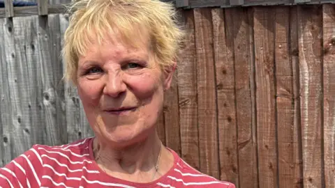 George King/BBC A head and shoulders image of Jane Gunsman. She is wearing a red and white striped t shirt and standing in front of a fence. She is looking into the camera.