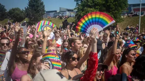 Huge crowds of festival goers pictured at Pride Canterbury in 2023. Someone in front is holding aloft a rainbow coloured fan   