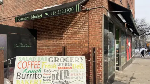 Danielle Kaye A sign advertising food and drinks stands in front of a brick building.