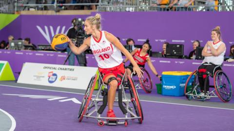 Amy Conroy on a purple court playing wheelchair basketball, wearing a white and red uniform 