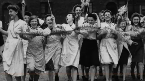 Women dance jubilantly waving Union flags 