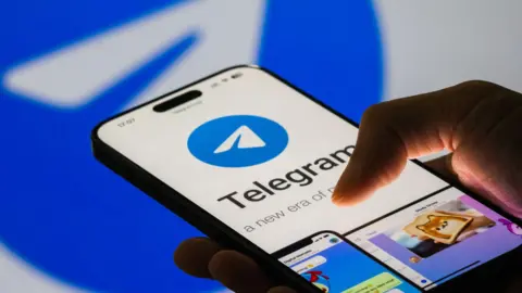 Getty Images Gambar close-up iPhone di tangan seseorang memperlihatkan layar Telegram dengan logo menyerupai pesawat kertas bergaya dalam lingkaran biru