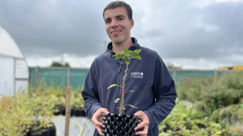 Assistant Sam Brown holds sapling tree at tree nursery