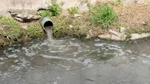 Water pours from a pipe into a river