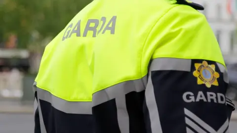 The back of a Garda member wearing a black and hi-vis yellow jacket. 