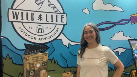 A woman poses in front of toys, and a sign reading "Wild Life Outdoor Adventures".