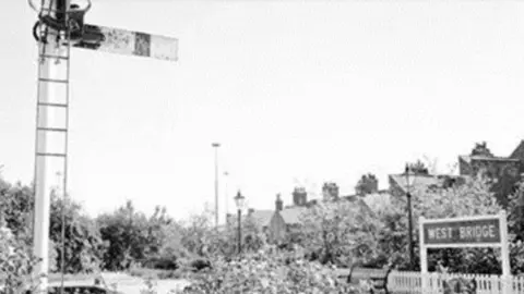 Leicester City Council A black and white image of the West Bridge station platform with a sigal post in the foreground.